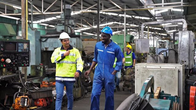 Engineers and employees walk inside the factory at break. Engineers and industrial workers are working on large machines.