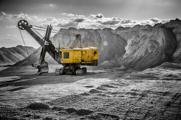 Yellow excavator standing among the rubble mountains in the black-and-white background.