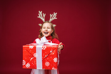Happy little girl 4 years old in reindeer antlers on a bright red background.