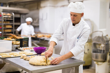 Portrait of man baker working with dough and forming baguettes - obrazy, fototapety, plakaty