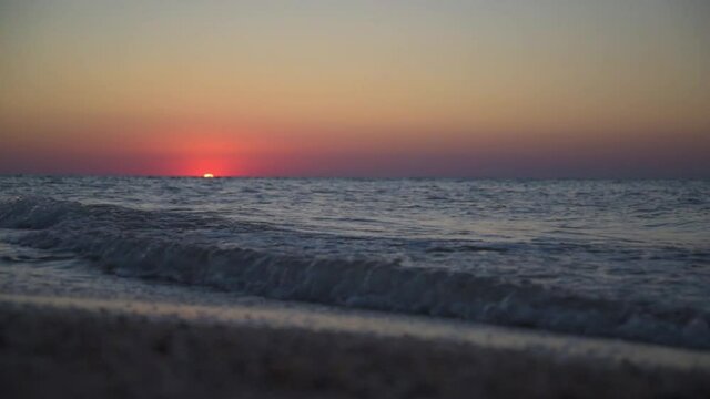 Calm picture of a sea sunset. The red sun sets in the sea. Incoming waves. The sky is colored red