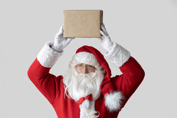 Santa Claus is standing and holding a box with a gift above his head.