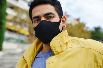 Young stylish man in yellow jacket in black protective mask poses outdoor.