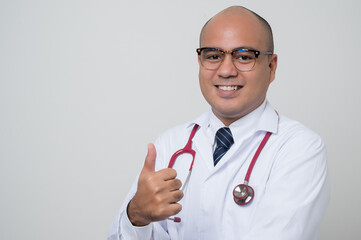 Doctor in white coat, stethoscope cross his arm and thumb up look into.camera with smile beside corner isolated on white background.
