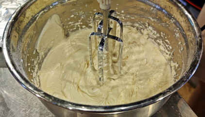 Making butter cream with sugar, butter, powder, eggs using electric hand whisk.