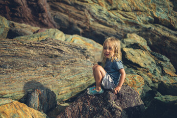 Naklejka premium Preschooler sitting on rocks on the beach