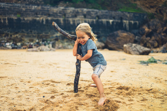 Preschooler using big stick to support himself in the wind on beach