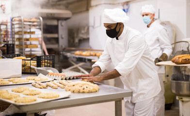 Baker at work in protective mask - making sweet buns with dough and eggs