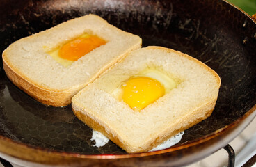 Eggs are fried in a pan with square bread.