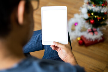 Closeup, People using the device home. A man sitting relaxed and holding a tablet white blank screen in the living room on weekends, Moke up, Clipping path. blurred background and Christmas tree.