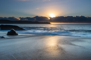 Fototapeta na wymiar Sunrise by the sea with cloud bank and sun rays on the horizon