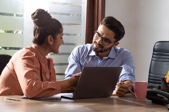 A YOUNG WOMAN AND MAN HAPPILY DISCUSSING WORK IN OFFICE	