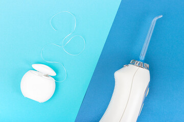 Dental floss and dental irrigator on blue background close-up, top view.