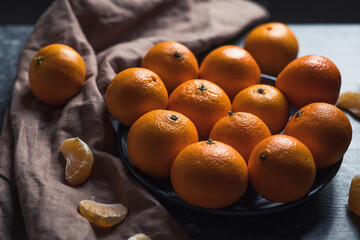 Round fresh ripe tangerines in a plate on a brown textile napkin. Low key. Vitamin C concept.