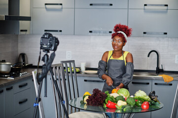 African american woman filming her blog broadcast about healthy food at home kitchen. She cuts a...
