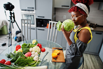 African american woman filming her blog broadcast about healthy food at home kitchen. She hold a...