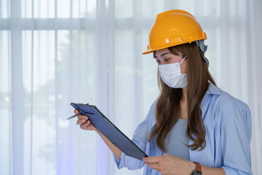 Female Engineer wear face mask with safety yellow helmet standing inside building check the correctness of the construction.