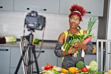 African american woman filming her blog broadcast about healthy food at home kitchen. She hold...