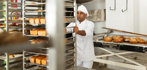 Baker transporting hot bread cart in bakery