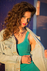 Beautiful young woman in a denim jacket on the background of a peeled purple wall. Girl with bright makeup in the style of the eighties on the street.