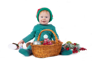 A beautiful Christmas kid with a basket filled with Christmas toys looks at the camera and smiles on a white background. Funny boy with Christmas tree decorations.