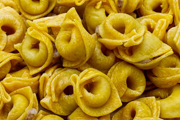Raw Tortellini in a wooden bowl on wooden table. Traditional italian pasta.  Closeup