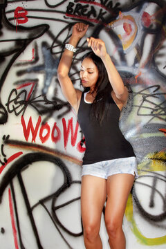 Mixed race woman dancing near graffitied wall