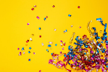 Colorful bright confetti and streamers on yellow background, top view. Copy space for text. Holiday mood, Christmas, New year, birthday or funny party
