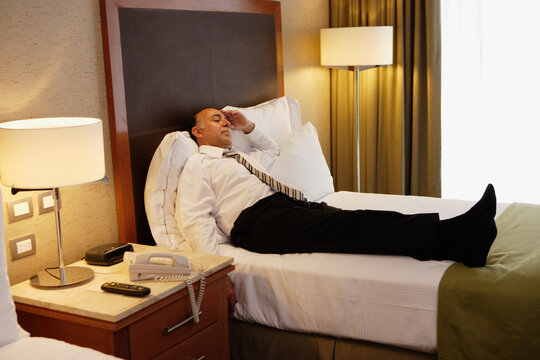 Middle-aged businessman laying on bed in hotel room