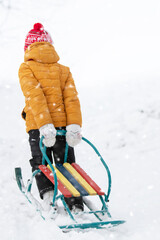 A child pulls a metal sled uphill in winter.