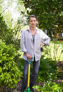 Woman leaning on spade in middle of her garden surrounded by bushes