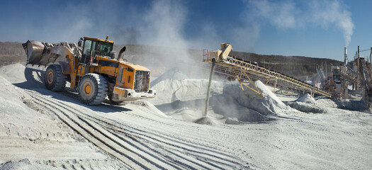 Front end loader near the stone crushing equipment at the limestone quarry, panoramic image. Mining...