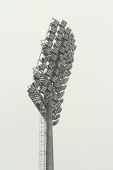 Stadium floodlight with metal pole, lighting mast, tower with floodlights in the sports stadium against the white sky.