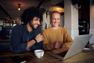 Handsome young man with beautiful woman looking at laptop screen in cafe and drinking coffee