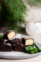 Glazed curds in chocolate with a mint leaf in a plate, on the background of pine branches