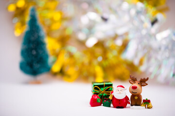 Santa Claus and reindeer figurines made of ceramic or resin. On a soft white background. Gold and silver background with blurred Christmas tree. Green gift box and golden bell.