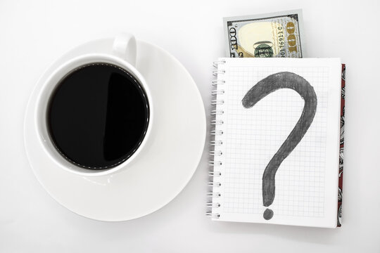 On a light background, a Cup of coffee with a Notepad with dollars and a question mark drawn next to it. The concept of finding solutions