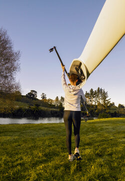Young woman carrying Kayak on her shoulder down to river edge