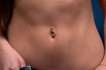 Close-up image of woman's slim belly with piercing