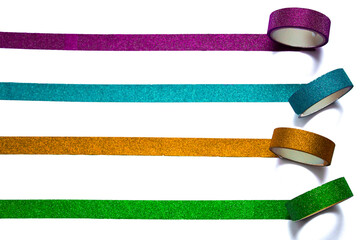 Four colorful rolls of washi tape unrolling horizontally on a white piece of paper. Selective focus