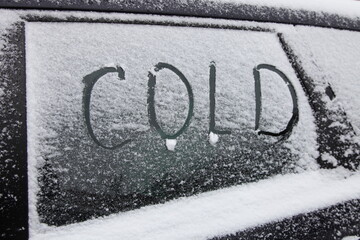 Inscription word COLD on snowy side car glass in winter day - driving safety, preparation for the trip, close up view winter concept symbol