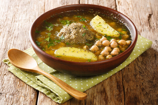 Authentic kufta bozbash meat soup with lamb meatballs, chickpeas, vegetables and herbs close-up in a plate on the table. horizontal