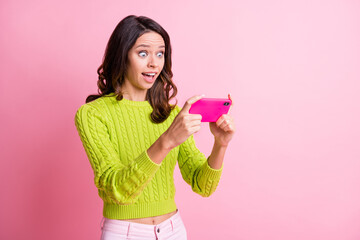 Photo of impressed wavy lady wear green sweater playing game modern device isolated pink color background