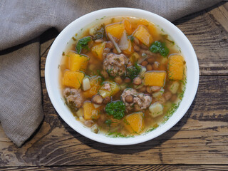 Pumpkin soup with meatballs and lentils in a white bowl with a napkin on a wooden background, top view. Recipe for seasonal autumn soup for proper nutrition
