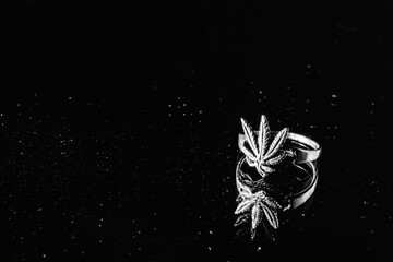 One silver cannabis ring lie on a black background with a mirrored surface. Silver occult jewelry