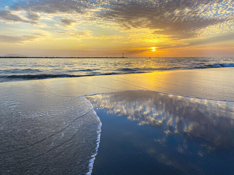 Orange beach sunset with cloud reflections on water and sand 