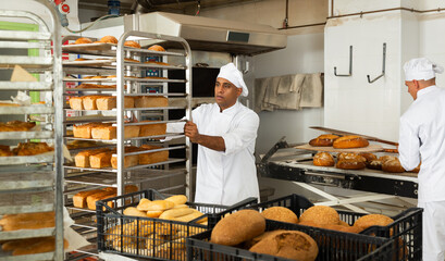 Portrait of man worker of bakery carrying rack trolley with freshly baked bread at kitchen