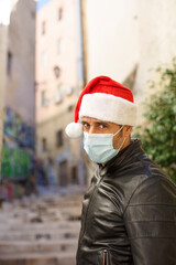 Uomo con cappello da babbo natale, giacca in pelle e mascherina chirurgica,  guarda triste in...