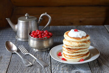 Stack of pancakes with sour cream is in front of silver utensils on the wooden background. 
