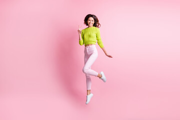 Full length photo of adorable curly woman dressed green pullover jumping showing v-sign isolated pink color background